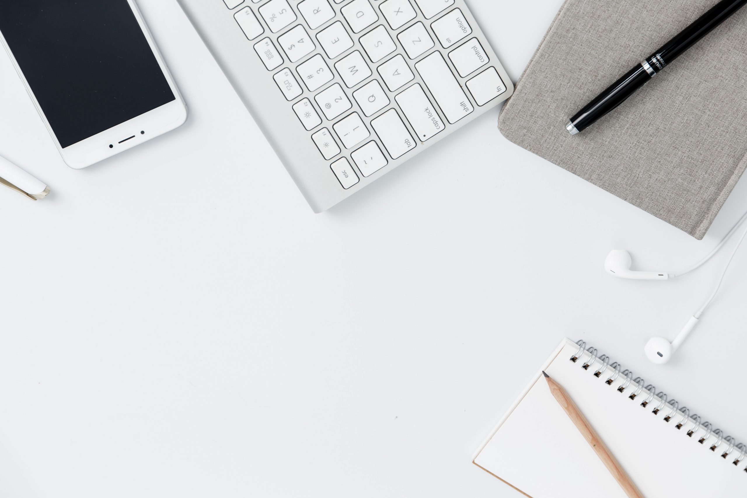 Birds Eye view of white desk with phone, keyboard, notepad, and pencil and pen