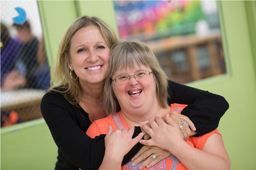 Two women, one an employee, one a client, hugging and smiling