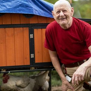 Man kneeling and smiling next to a chicken coop.