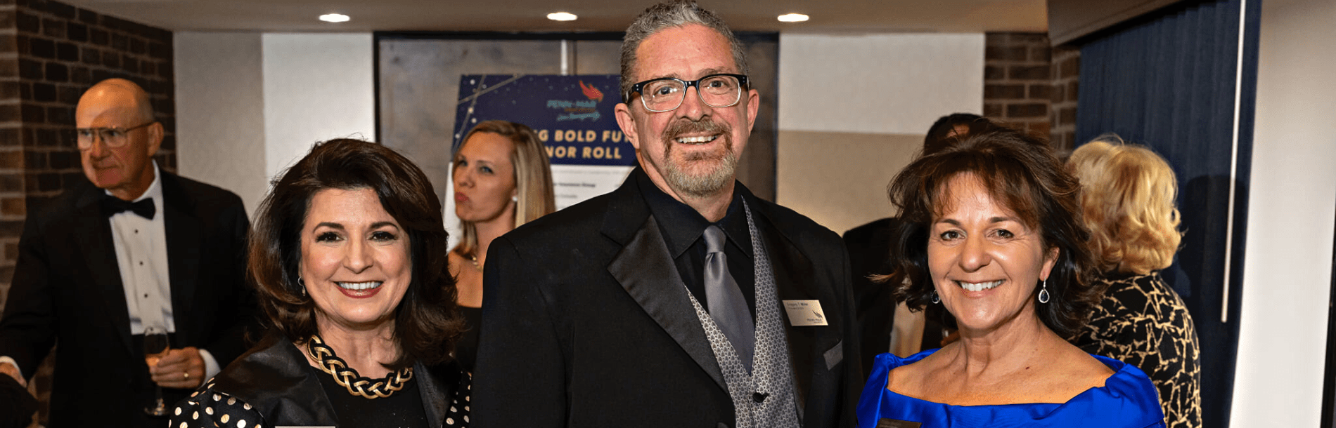 Two women and a man in the middle smiling at a formal event.