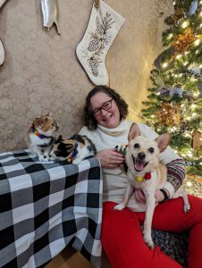 Woman smiling with her two cats and a dog next to a christmas tree.