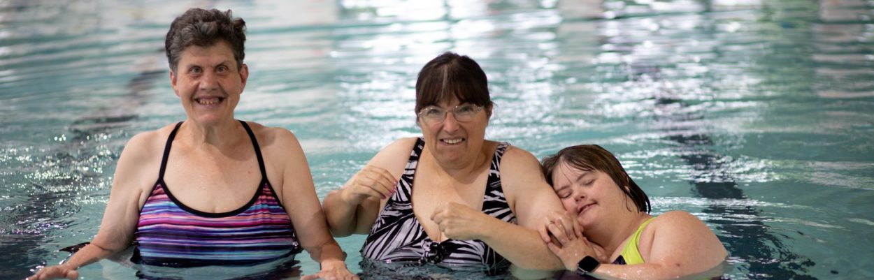 3 women in a pool smiling together.