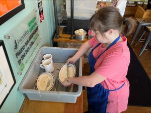 A woman working at a bakery taking care of dirty dishes.