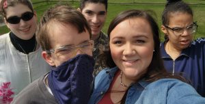 5 people smiling while taking a group selfie outdoors.