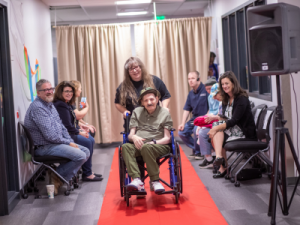 A man in a wheelchair being pushed down a fashion runway.