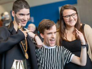 Two men and a woman posing for a picture behind the scenes of a fashion show.