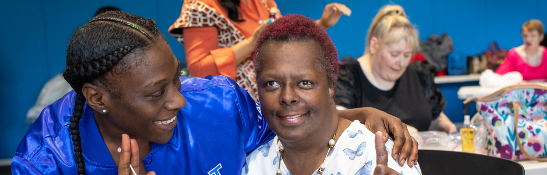 A woman smiling with her finger up and a woman next to her smiling and looking at her.