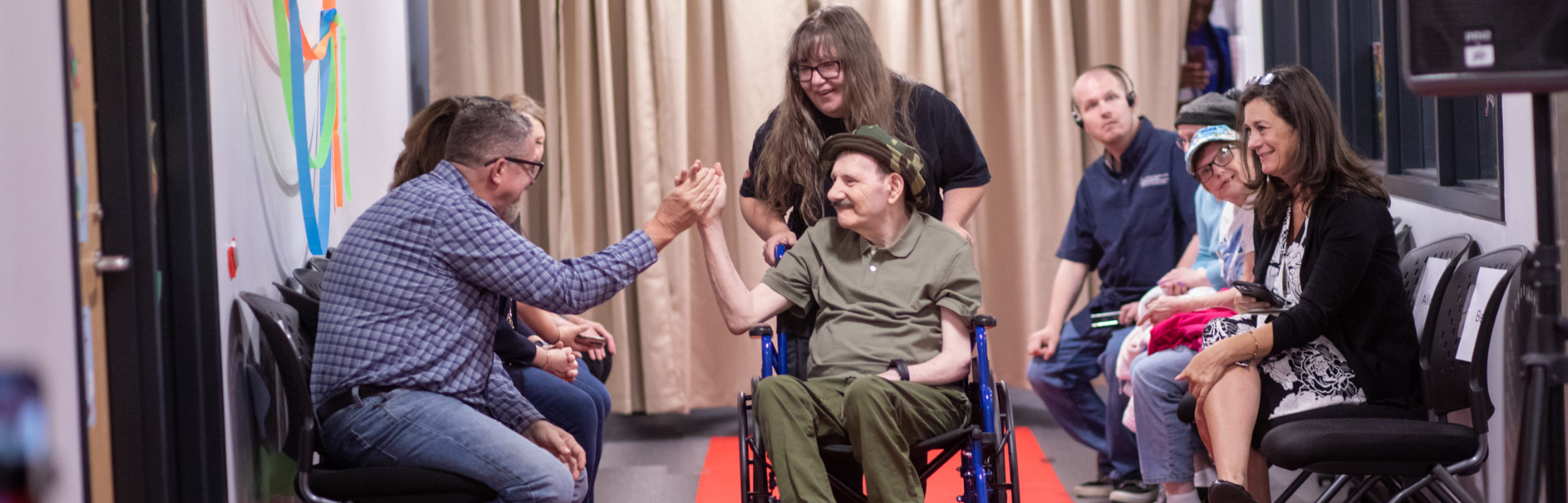 A man in a wheelchair giving a high five to a man sitting next to him with his DSP behind his wheelchair.