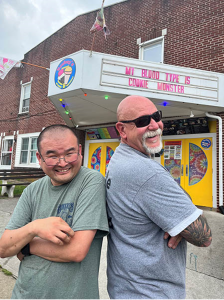 Two men standing back to back in front of an ice cream shop.