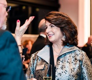 A woman smiling talking to a man at a formal black tie event.