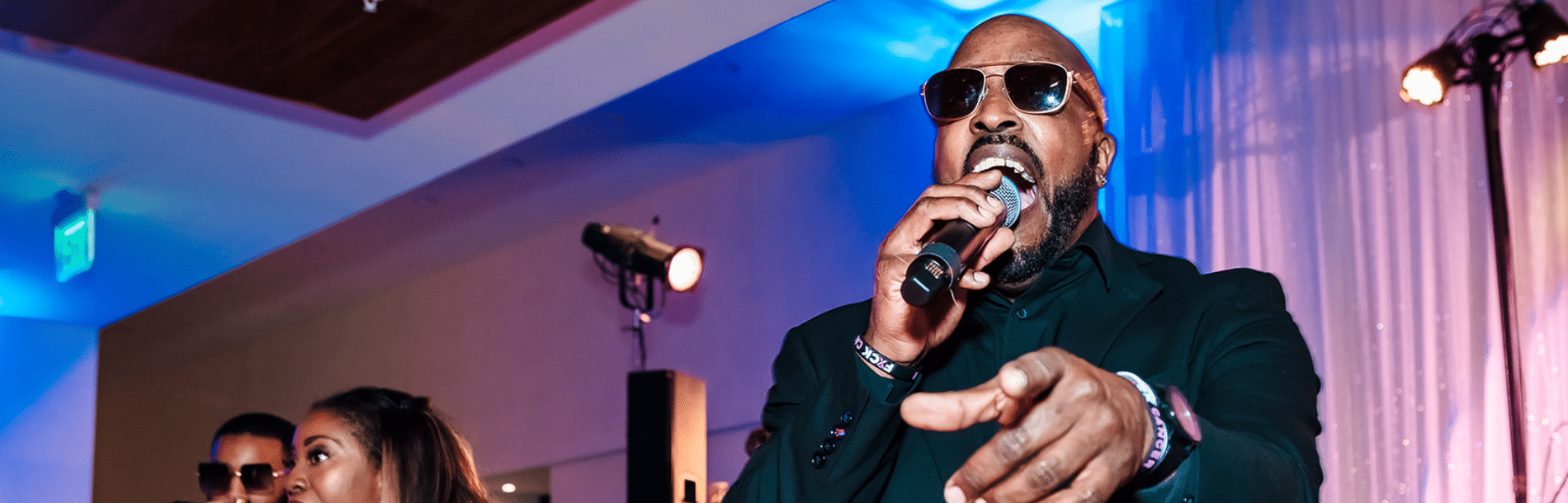 A man singing into a microphone and pointing at the camera.