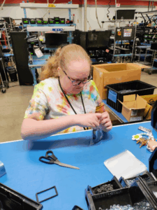 Gabby sits at a table at her job working with her hands.