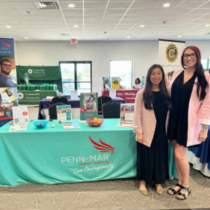Danielle Gattine and another Penn-Mar team member stand next to a table with Penn-Mar branded information about Customized Employment and Pre-ETS services offered.
