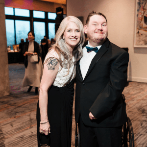 Kari Ebeling and Bill Wagaman, a person supported by Penn-Mar, smile and pose together, both dressed in formalwear, at the Gala.