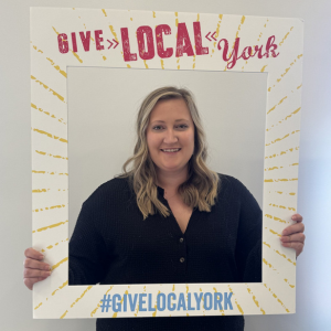 Charmaine Nyman holds a cardboard cutout Give Local York frame around her.