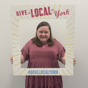 Alexa Wheeler holds a cardboard cutout Give Local York frame around her.