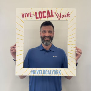 Jorgen Post holds a cardboard cutout Give Local York frame around her.