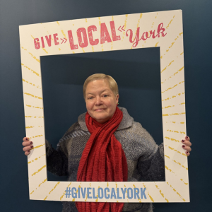 Lesley Redmond holds a cardboard cutout Give Local York frame around her.