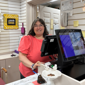 Lisa smiles at the camera while standing behind the cash register in the gift shop.