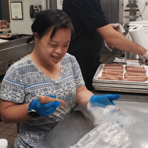 Miriam smiles as she prepares food in a kitchen.