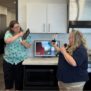 Aime Newton (left) helps coworker Allis Kensing demonstrate an Assistive Technology tool.