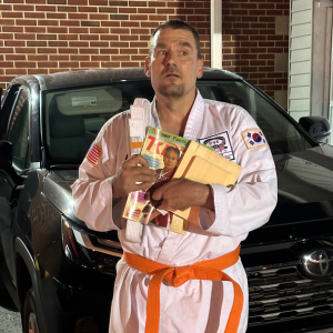 Robert Zerance holds papers in his hands while dressed in a martial arts uniform with an orange belt.