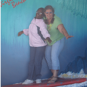 Michelle poses on a surfboard photo backdrop with another person.