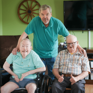 Three men, two sitting and one standing, pose together in a living room.