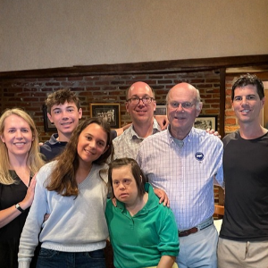 A family of seven people pose together in front of a brick wall.